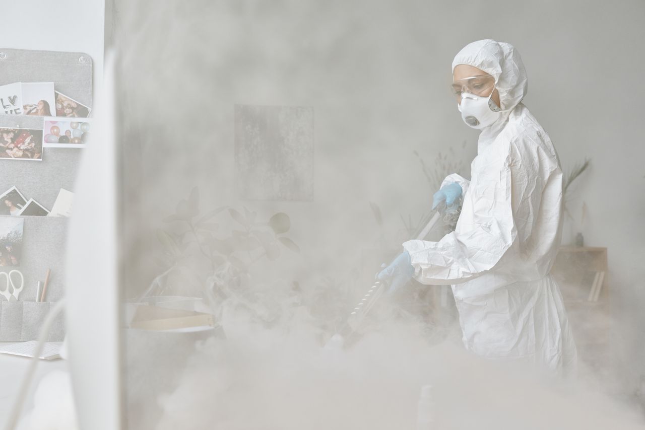 Une femme en combinaison de protection désinfecte un espace intérieur à l’aide d’un équipement de brouillardage.